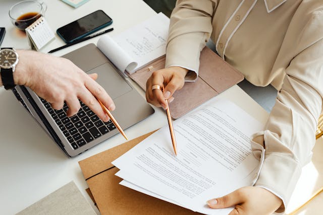 two-people-working-at-desk-with-laptop-and-papers